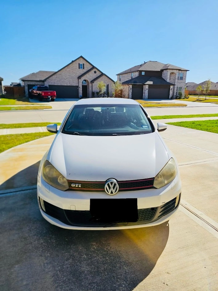 White Volkswagen GTI parked in a residential Houston driveway, ready for pickup—illustrating how easy it is to sell your junk car with free towing and recover space.