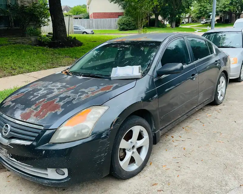 Gray damaged junk car parked in a driveway in The Woodlands, TX, ready for fast cash pickup and free towing by 832 Cash For Junk Cars Houston.
